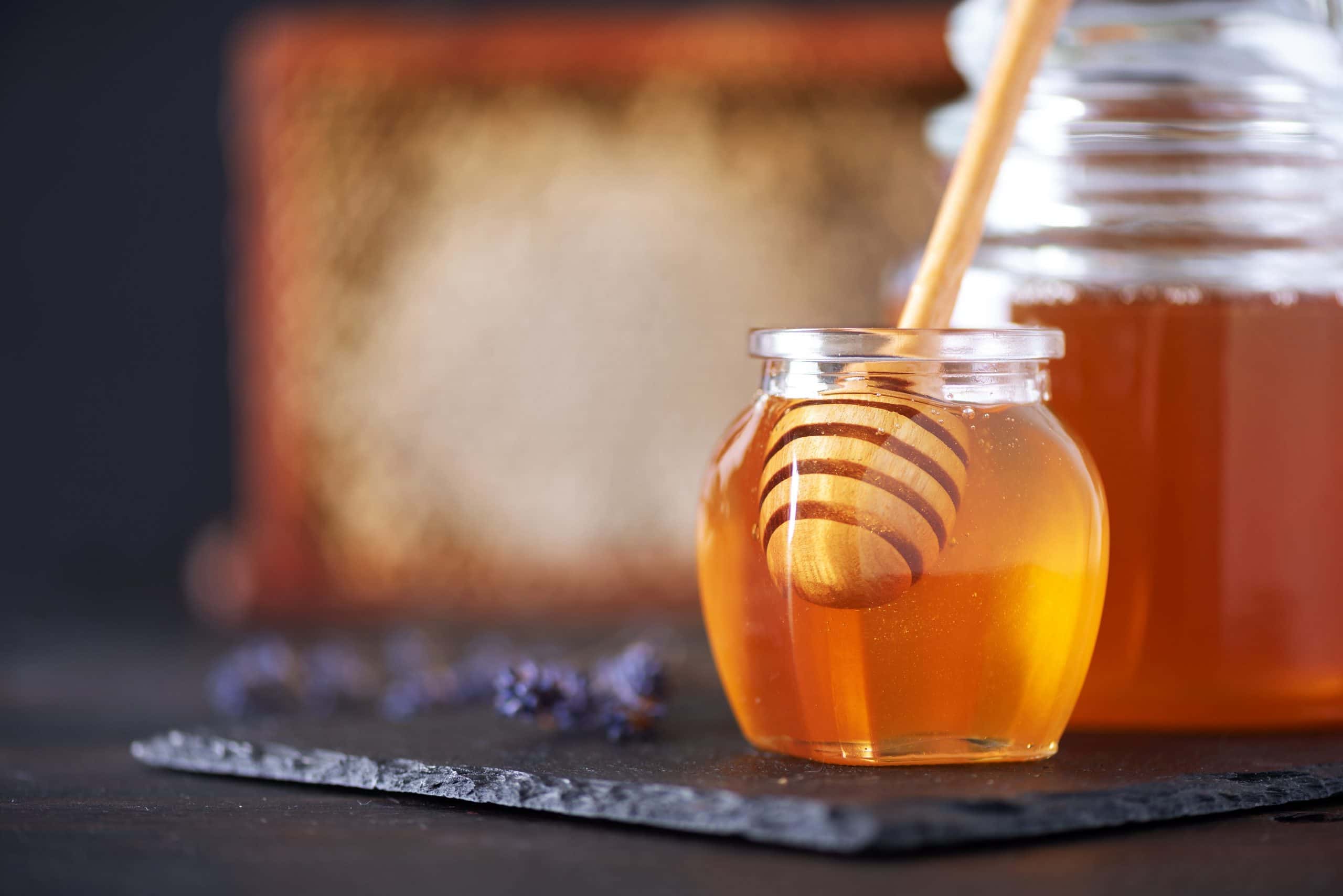 small jar with honey and a honey dipper on a black plate with a bigger glass jar in the background