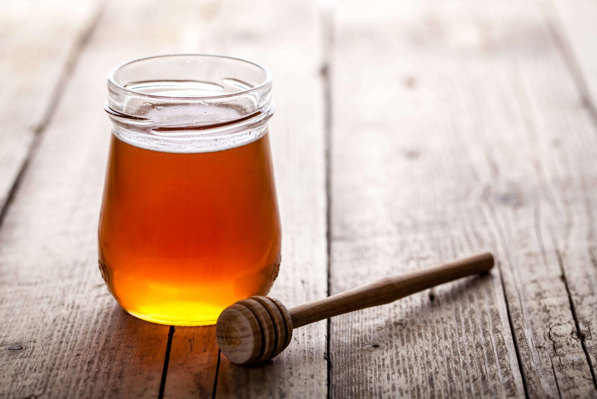 glass jar of mad honey on a wooden table with a honey dipper laying next to it