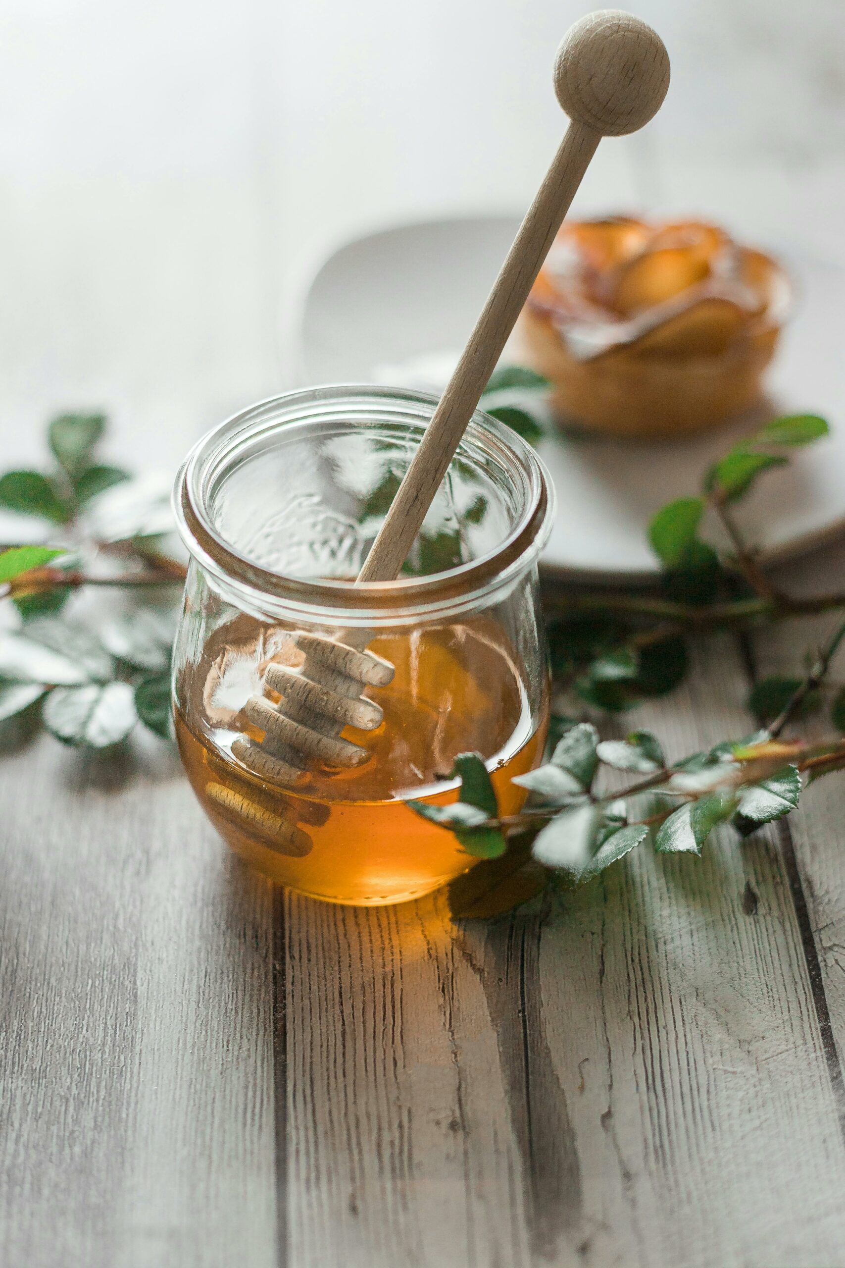 Honey in a small cup with a wooden stick and small leaves on the table